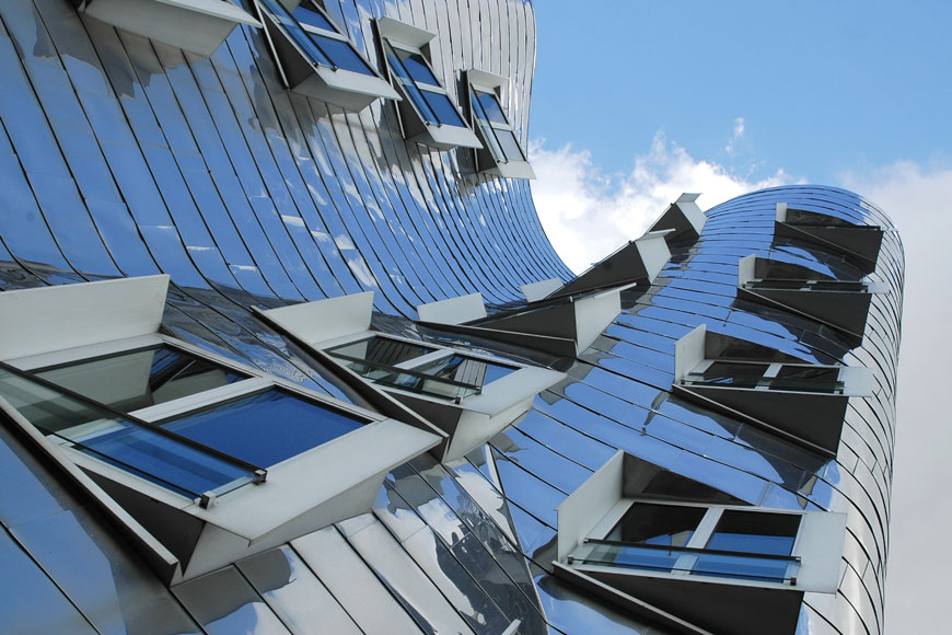 A stainless steel clad modernist building with curved walls reaches towards a blue sky.