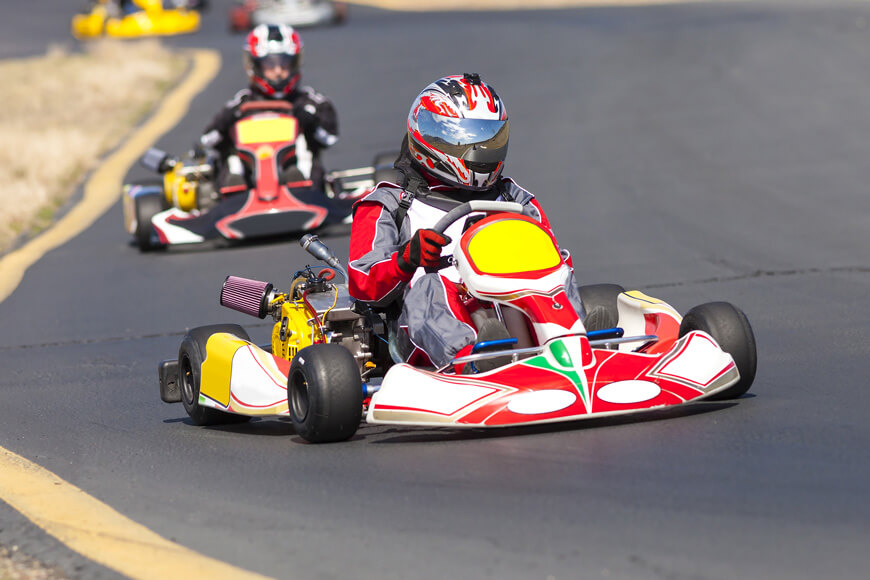 Go-kart racers are racing past the corner of the race track