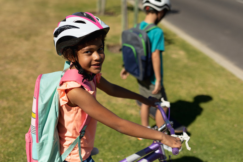 A cute elementary school child on a bike grins up at the camera