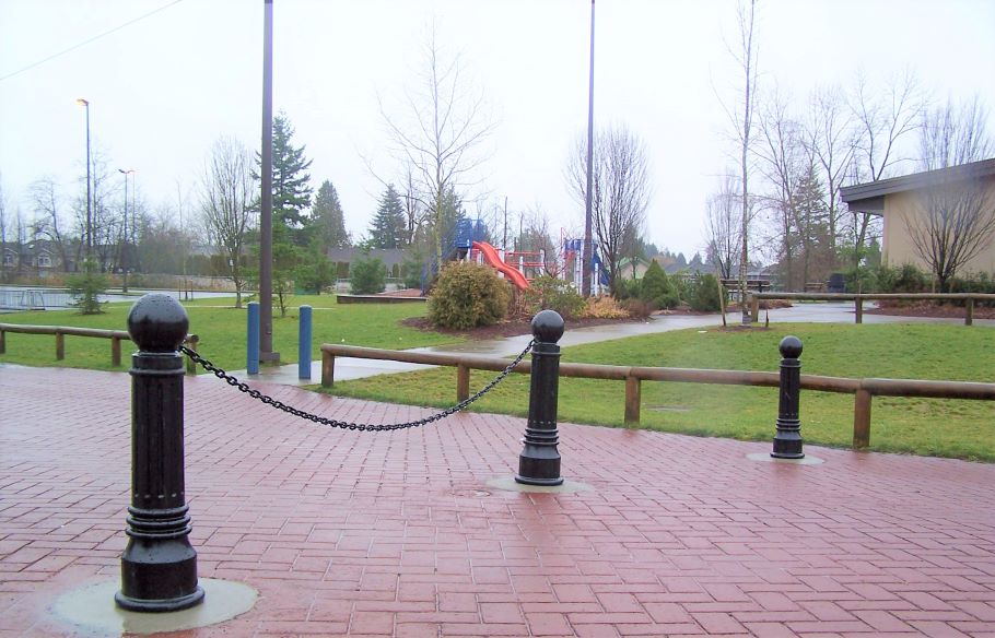 Three black bollards linked by chains stand near a school playground