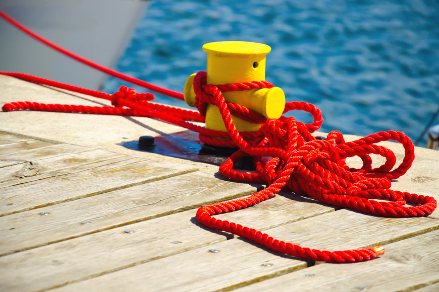 A short yellow mooring bollard is lashed with vibrant red rope beside a choppy sea