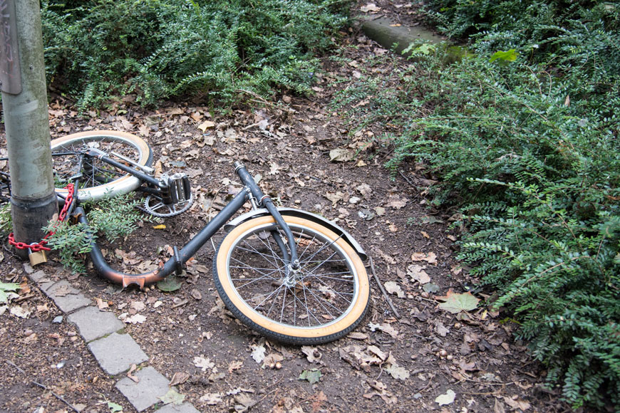 A badly vandalized bike is chained to a lamp post.