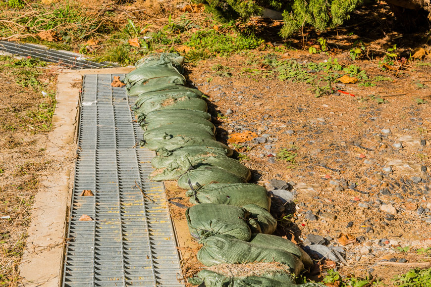 A row of sandbags sits behind a drain in a ditch