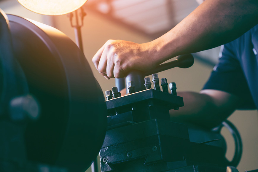 A worker uses a lathe grinder in a metal shop