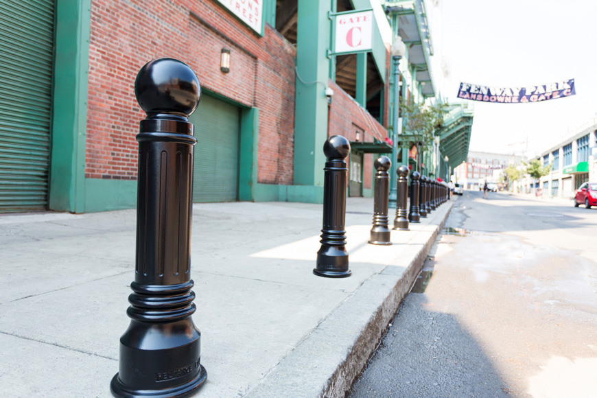 A banner announcing “FENWAY PARK” floats over a city street lined with bollards