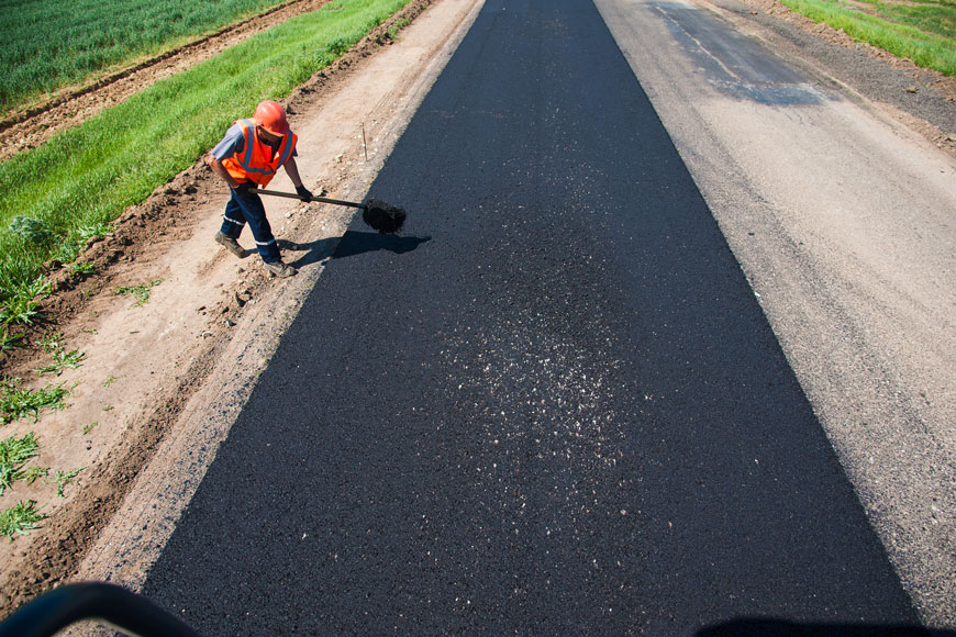 Construction worker uses shovel to move asphalt