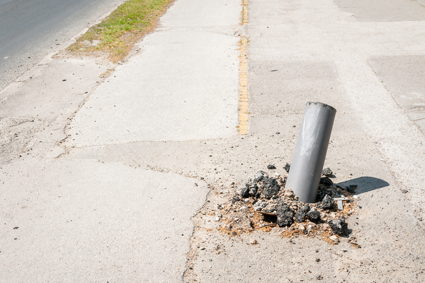 A bollard lies on an angle, having been pulled from the surrounding cement