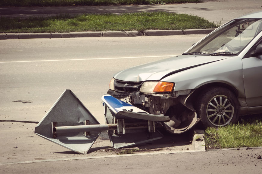 A car with a crumpled hood sits on top of a median and crumpled sign.