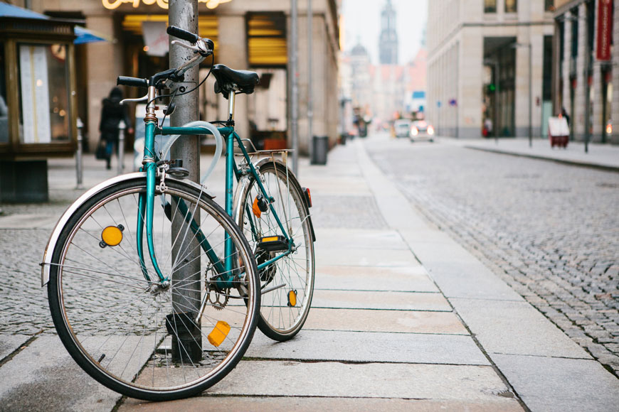 Vélo bleu verrouillé sur un poteau en métal avec un câble antivol dans une rue européenne