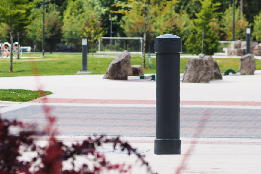 A gray bollard with a gently-domed cap sits behind a spray of bright red leaves