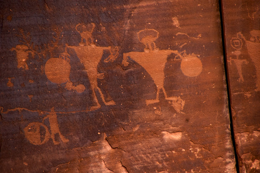 On a dark red clay wall, two images of two warriors with spears and horns are scratched into the surface