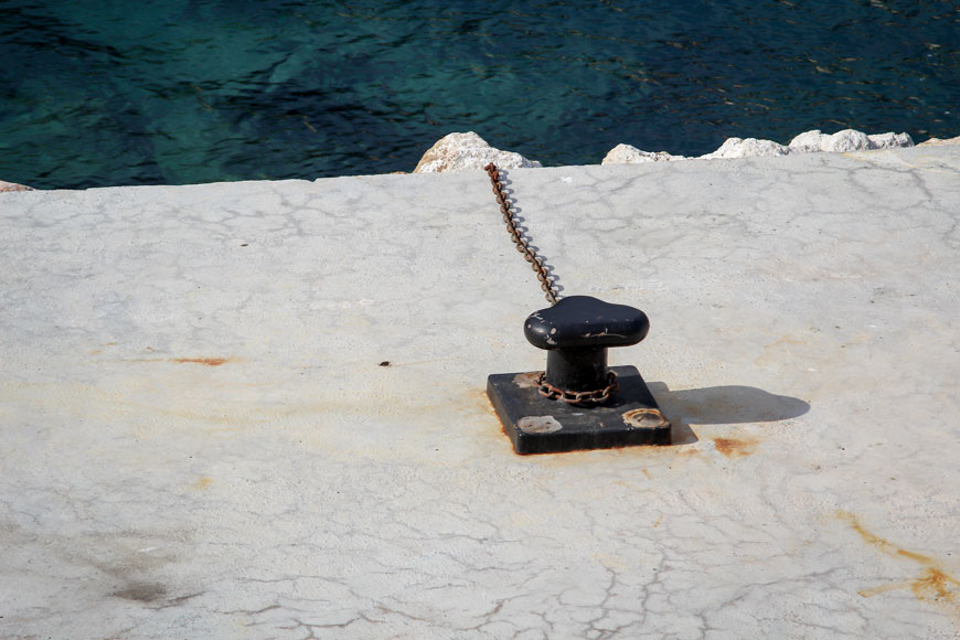 A T-bollard is bolted to a dock and wrapped with a thick chain