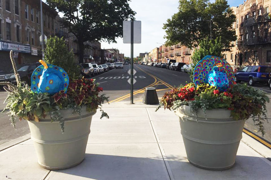 Martello bollard stands between concrete planters filled with plants and street art