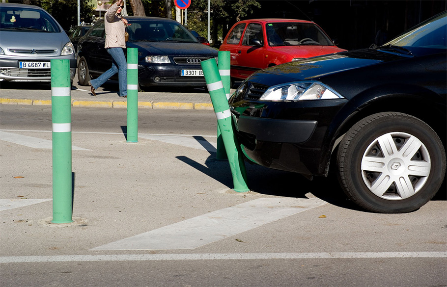 A black sedan colliding into a bumper post in a parking lot