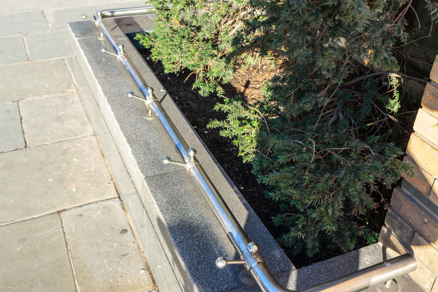 A steel bar with pointed knobs prevents skateboarders from sliding across a worn stone curb