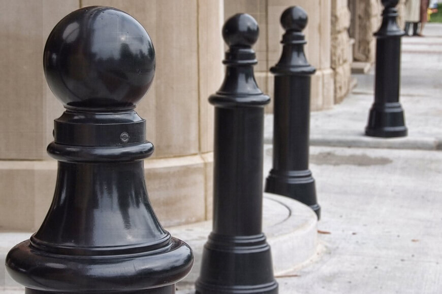 Numerous black bollards in a line on a sidewalk