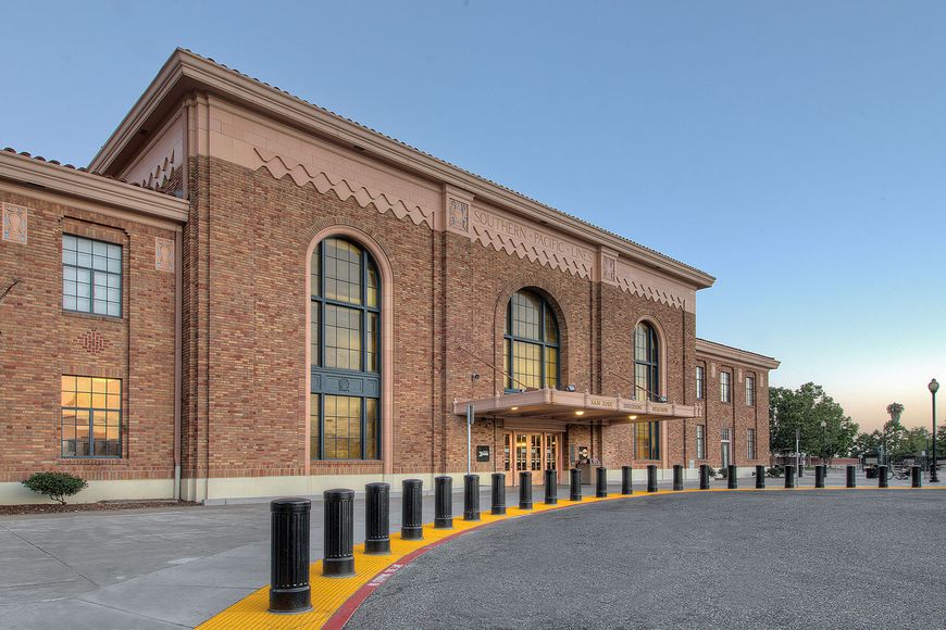 10-inch pipe bollards covered by fluted decorative steel bollards in front of a yellow brick train station